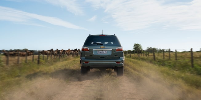 Imagem do novo SUV Chevrolet Trailblazer High Country, cinza topázio, andando em uma estrada de terra, em ambiente rural.