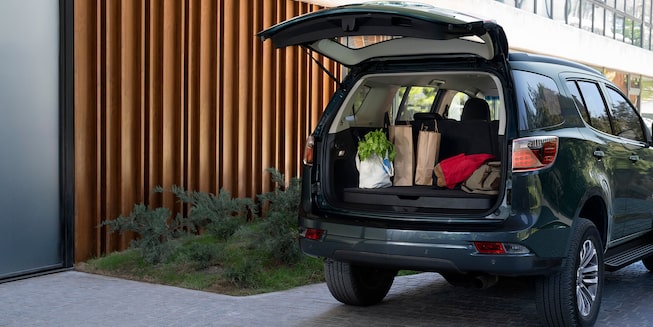 Imagem mostrando novo SUV Chevrolet Trailblazer estacionado em frente a uma casa, com o porta malas aberto e com produtos dentro, destacando o espaço do bagageiro.