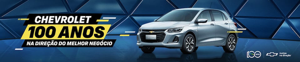 Um carro Chevrolet cinza é exibido contra um fundo azul geométrico. O texto diz Chevrolet 100 Anos: Na direção do melhor negócio com logotipos Chevrolet e símbolos comemorativos.