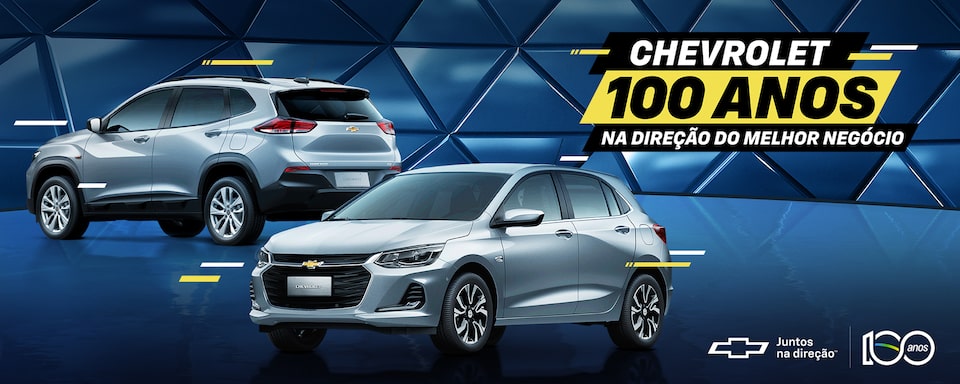 Dois carros Chevrolet, um SUV prateado e um hatchback prateado, são exibidos em um fundo geométrico azul. O texto diz Chevrolet 100 Anos na direção do melhor negócio comemorando 100 anos. Os logotipos estão incluídos na parte inferior.