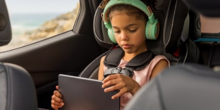 Imagem de uma menina no banco traseiro de um veículo Chevrolet, usando um tablet.