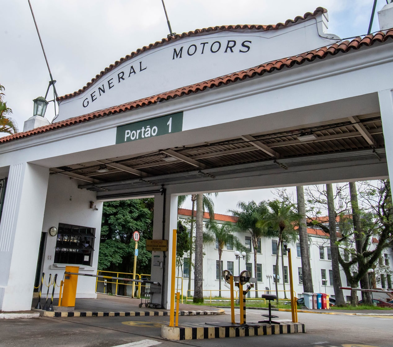 Entrada principal da fábrica da General Motors em São Caetano do Sul, com portão branco identificado como Portão 1 e letreiro General Motors no topo.
