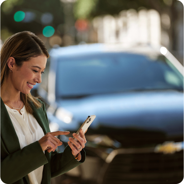 Mulher sorrindo e utilizando o celular em frente a um Chevrolet.